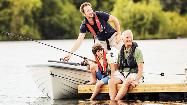 Three people sitting on a dock with a boat beside them